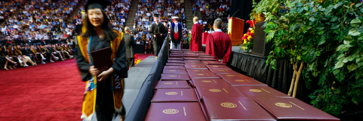 UMN graduate walking by tables with diplomas 